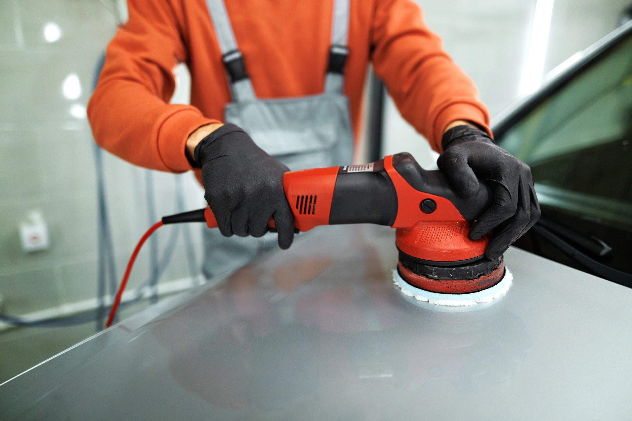 Detailer polishing a car hood with a rotary polisher.