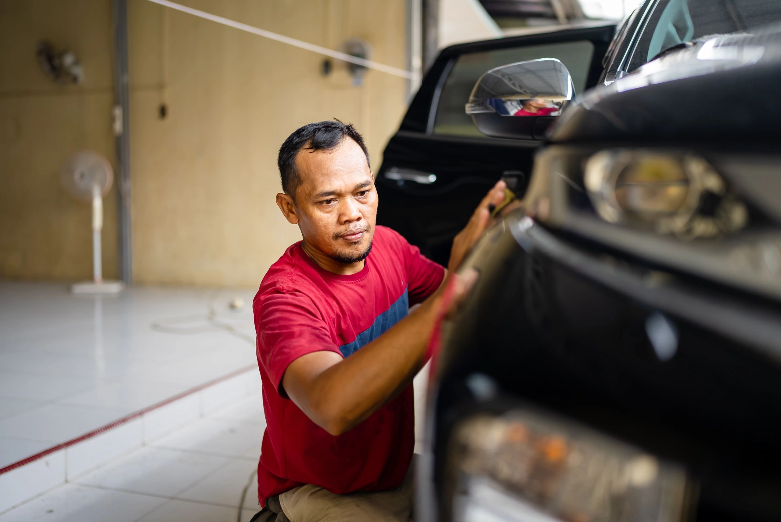 Auto detailer polishing a car door with an electric buffer.